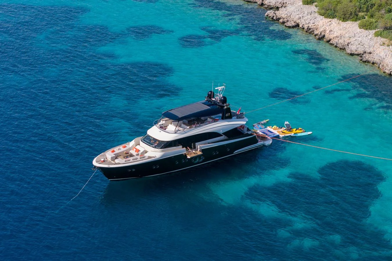 A luxurious yacht is anchored in clear turquoise waters near a rocky shoreline. aboard BELLA LUNA Yacht for Sale