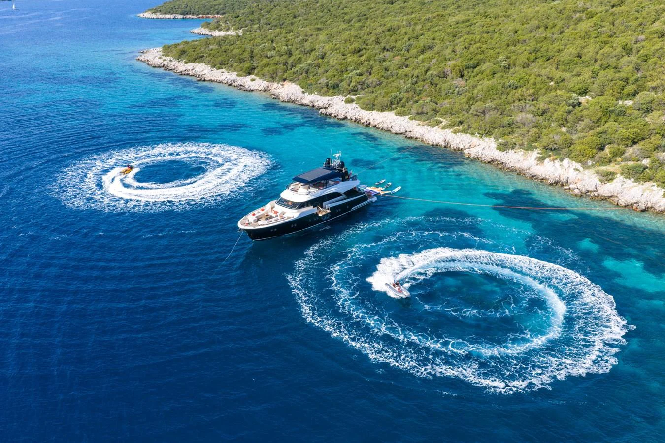 A luxurious yacht is anchored in a stunning coastal area with vibrant blue waters and lush greenery. aboard BELLA LUNA Yacht for Sale