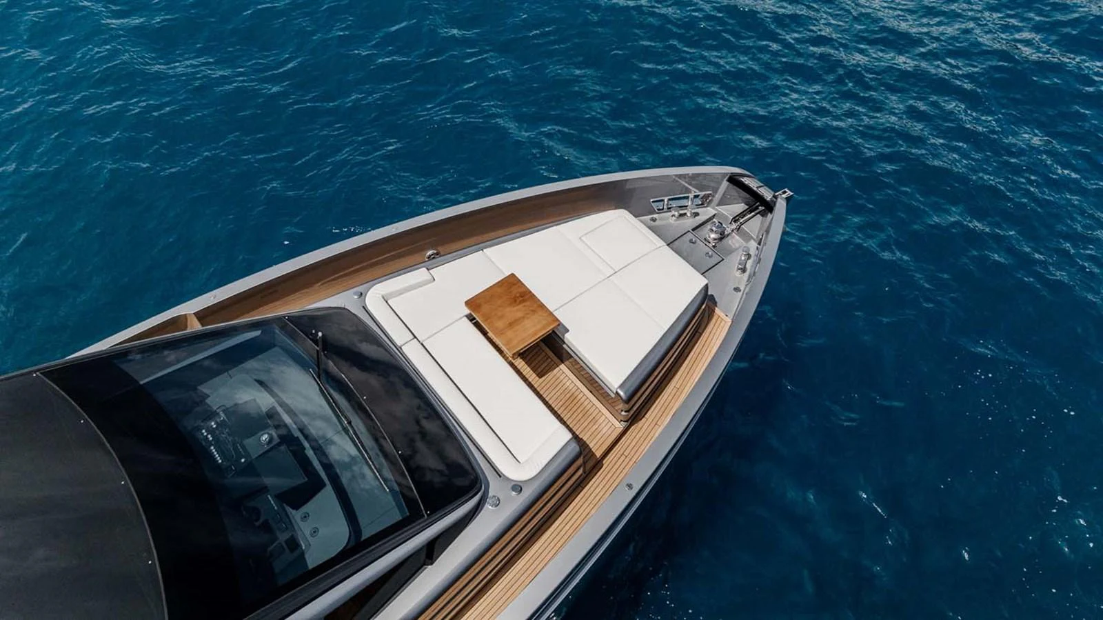 The sleek foredeck of the yacht features a stylish sunbathing area with plush cushions and a wooden table, set against the backdrop of the open sea. aboard REEMA Yacht for Sale