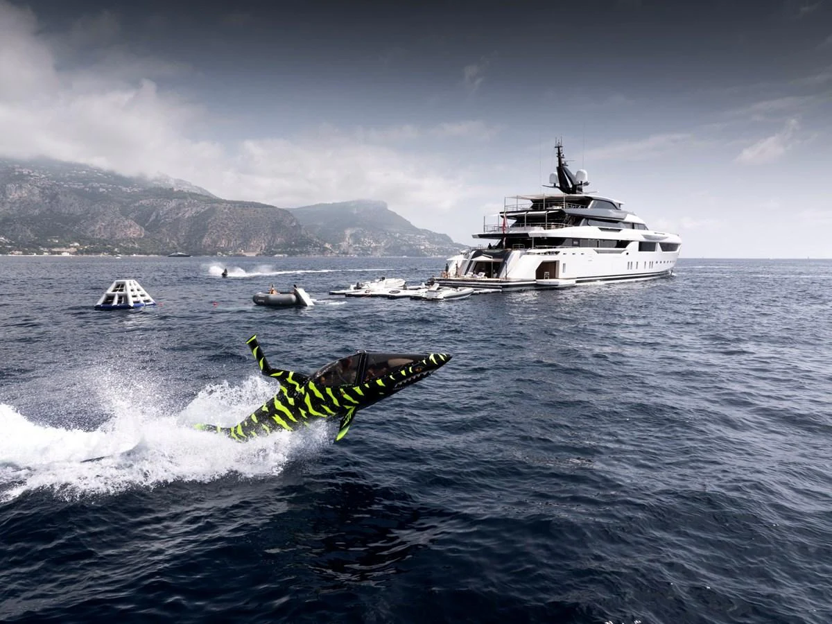 A sleek yacht is anchored in calm waters with a dynamic watercraft speeding nearby. aboard MALIA Yacht for Sale