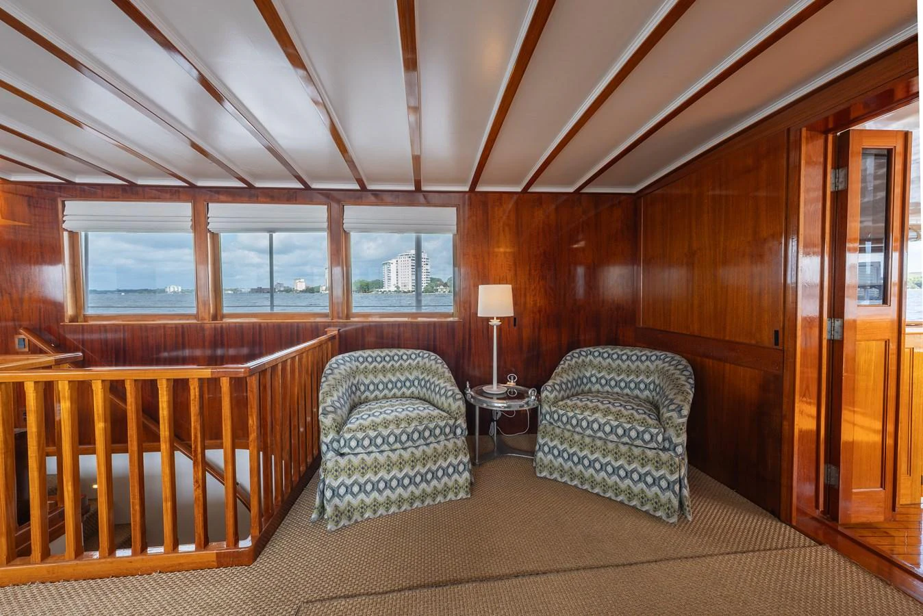 This cozy interior space features two patterned armchairs and a lamp, with large windows offering a scenic view. aboard INNISFAIL Yacht for Sale