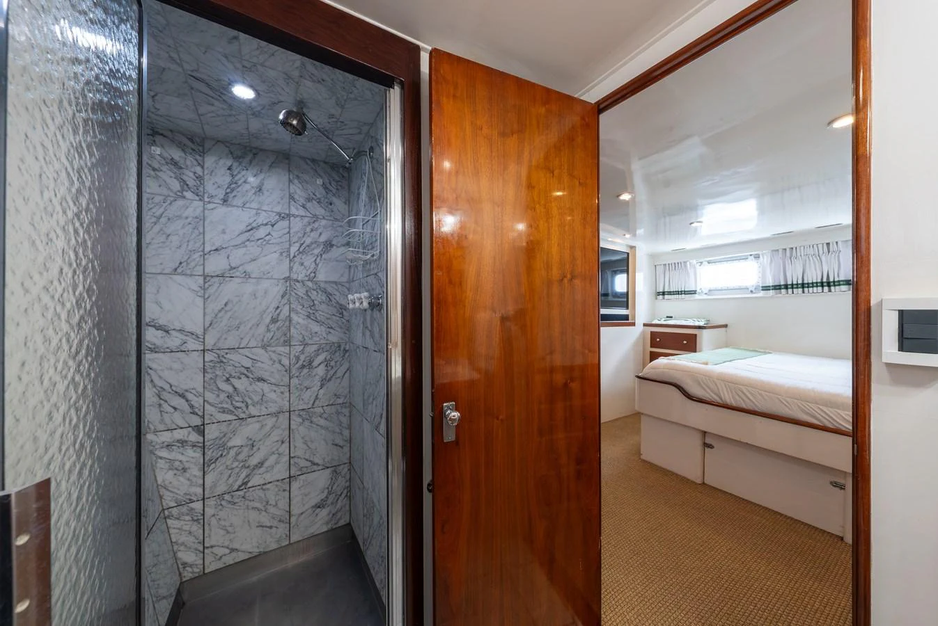 The image showcases a cozy stateroom with an adjacent marble-tiled shower area. aboard INNISFAIL Yacht for Sale