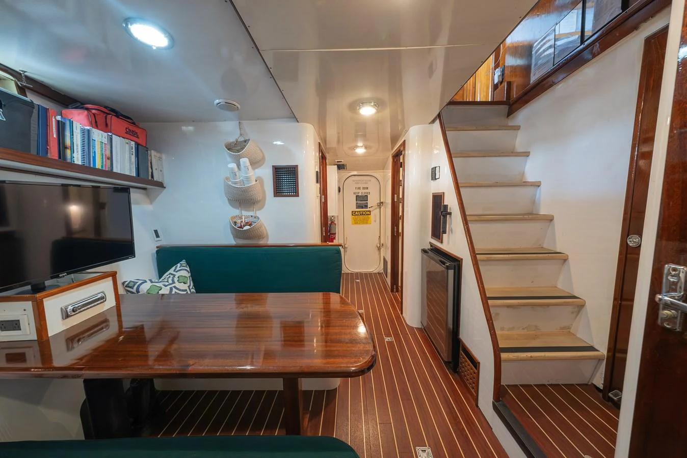 The yacht's interior features a cozy dining area with a wooden table, green seating, and a staircase leading to the upper deck. aboard INNISFAIL Yacht for Sale