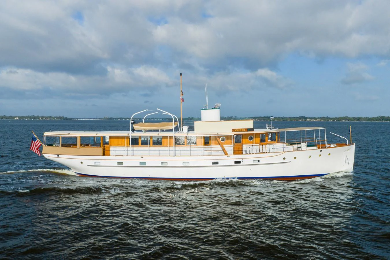 A classic yacht cruises gracefully on open waters under a partly cloudy sky. aboard INNISFAIL Yacht for Sale