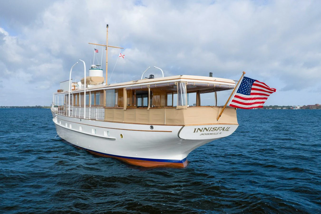 A classic yacht with elegant lines cruises smoothly on the open water under a partly cloudy sky. aboard INNISFAIL Yacht for Sale