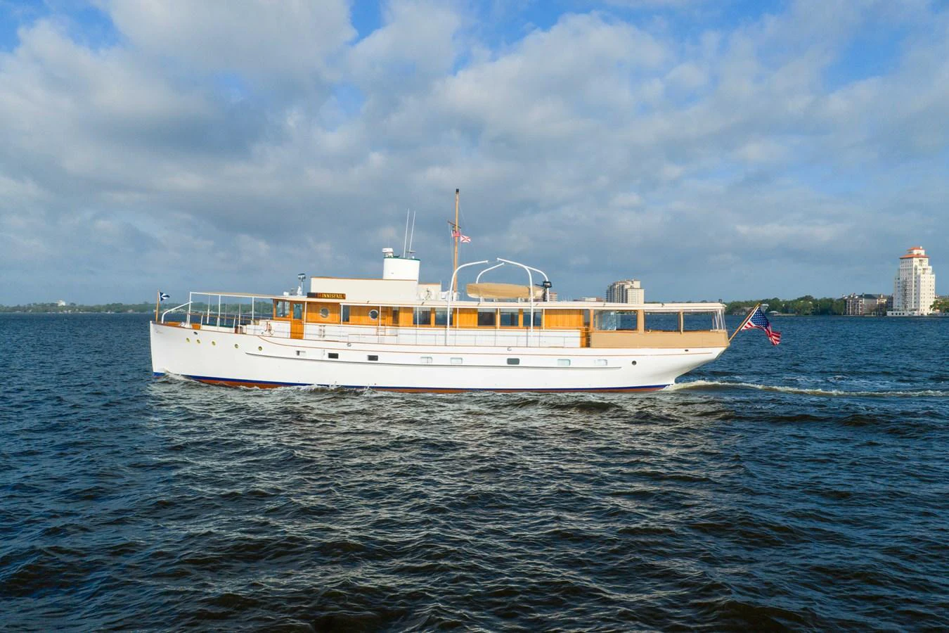 A classic yacht cruises gracefully on open waters under a partly cloudy sky. aboard INNISFAIL Yacht for Sale