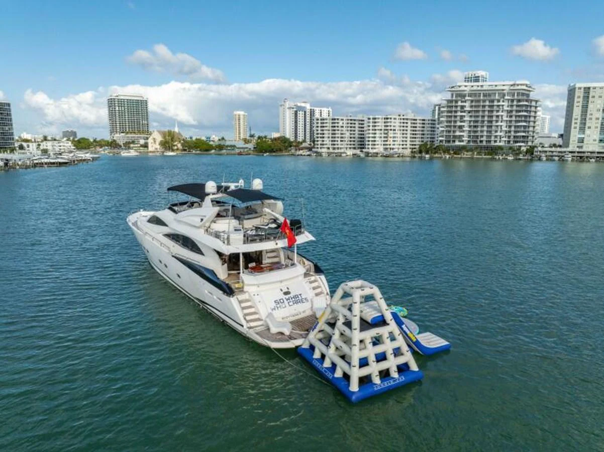 A luxurious yacht anchored in a serene harbor with an inflatable water toy attached at the stern. aboard SO WHAT WHO CARES Yacht for Sale