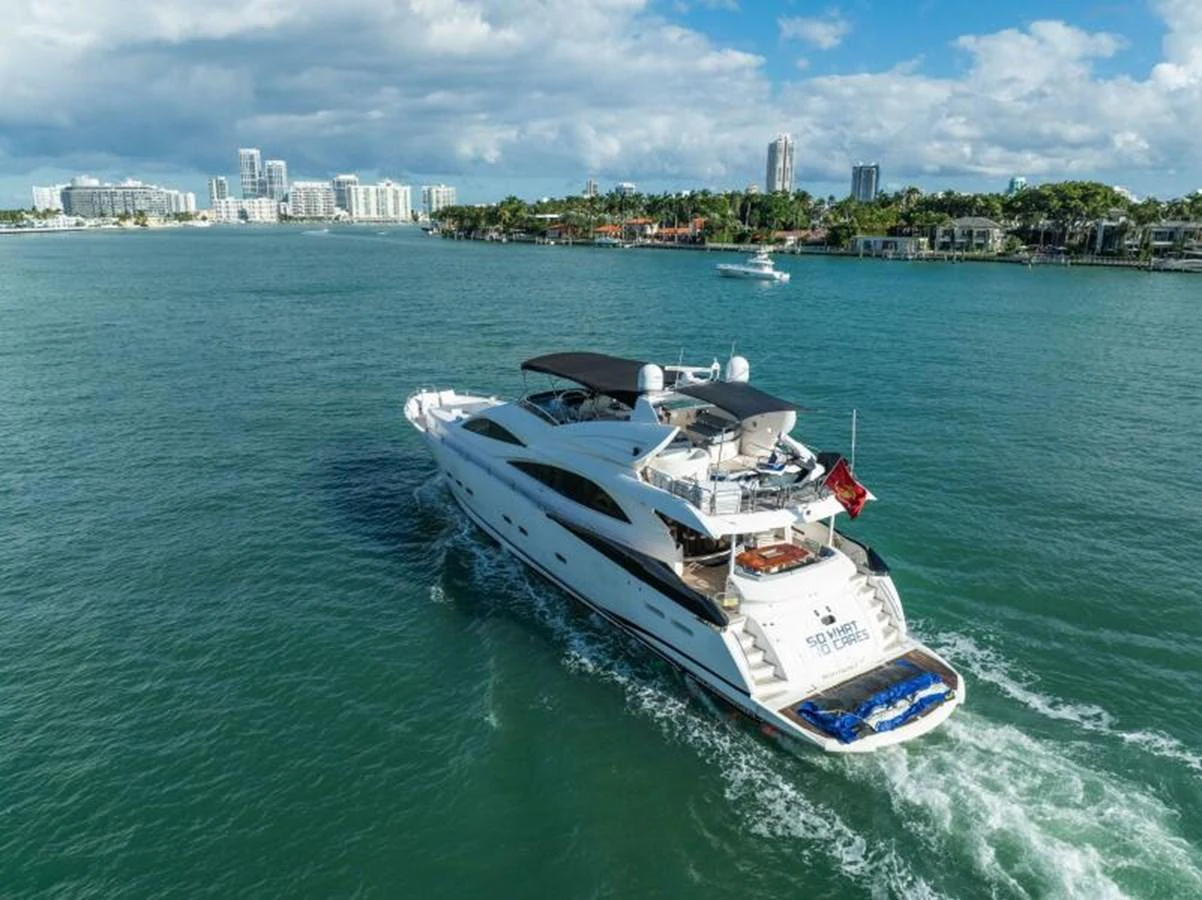 A luxurious yacht cruises through a scenic coastal area with a city skyline in the background. aboard SO WHAT WHO CARES Yacht for Sale