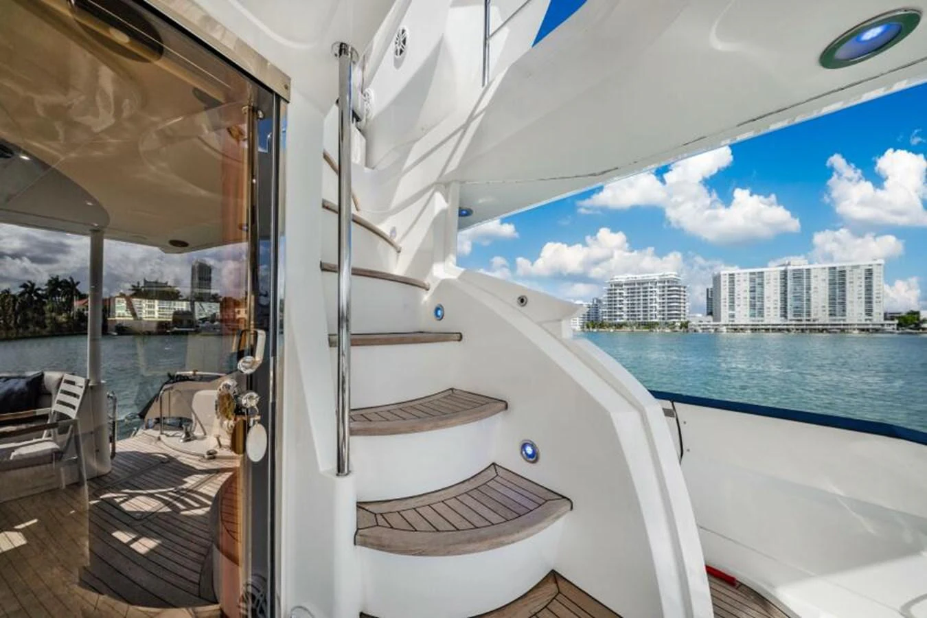 The yacht's aft deck features a stylish staircase leading to the upper levels, with a view of the surrounding waterfront. aboard SO WHAT WHO CARES Yacht for Sale