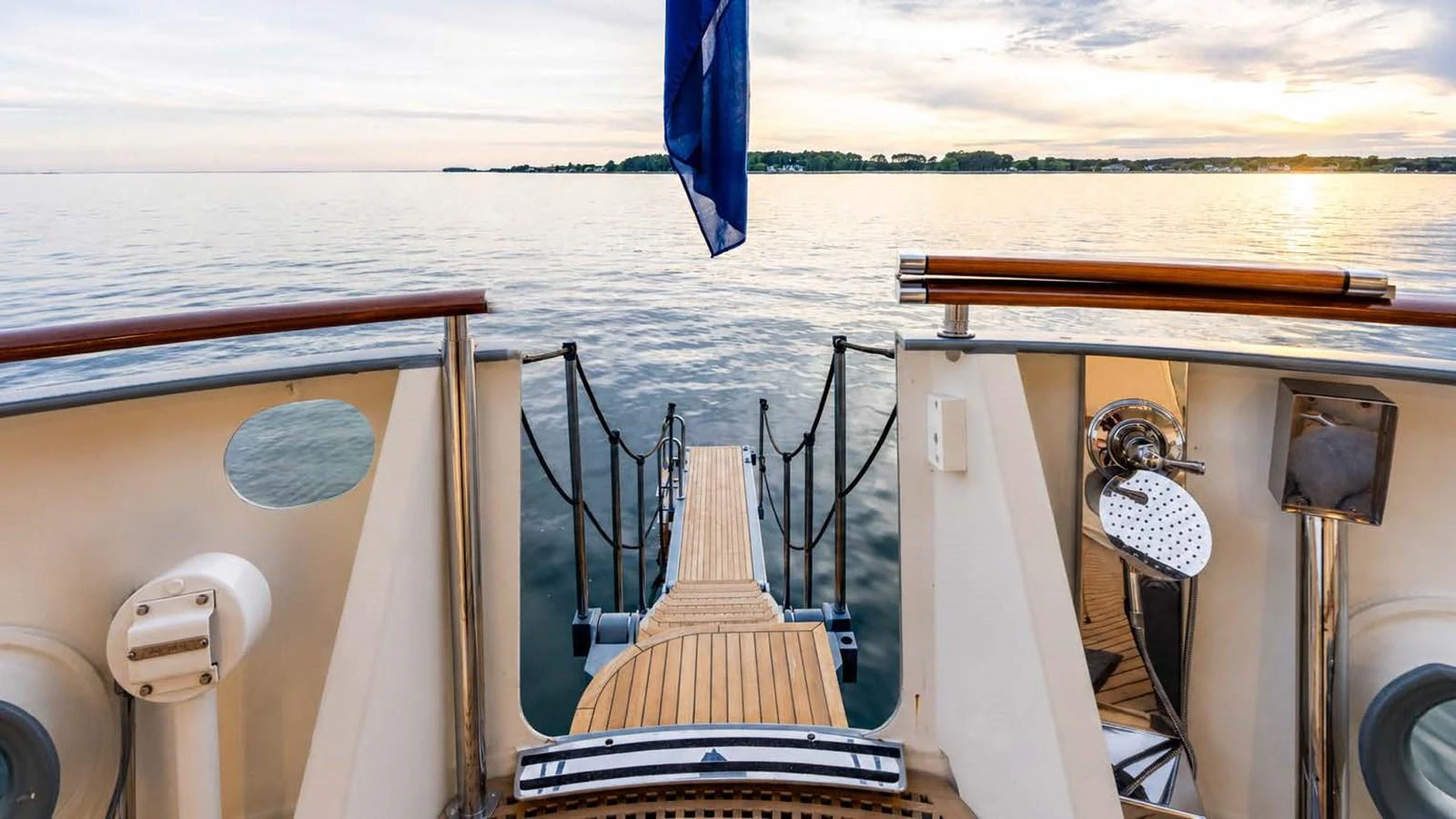 The aft deck offers a serene view of the water with a wooden gangway leading to the sea. aboard JUST B Yacht for Sale