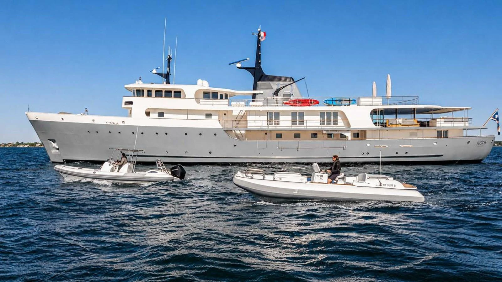 A sleek and elegant yacht cruising on the open water, accompanied by two tenders. aboard JUST B Yacht for Sale