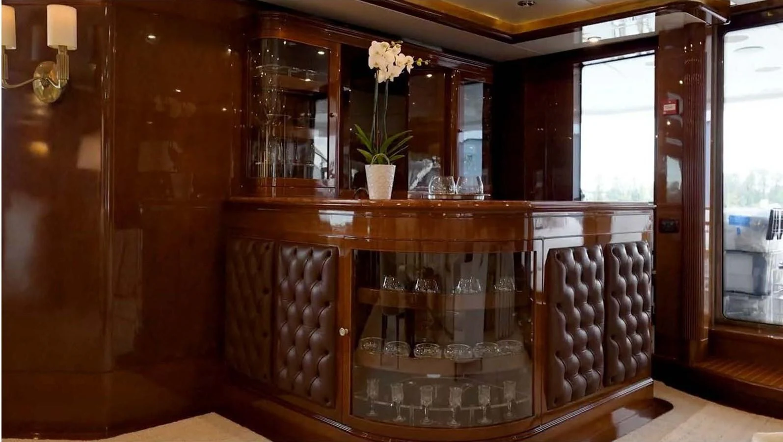 The yacht's interior features a luxurious bar area with rich wood finishes and elegant glassware displays. aboard DOMANI Yacht for Sale