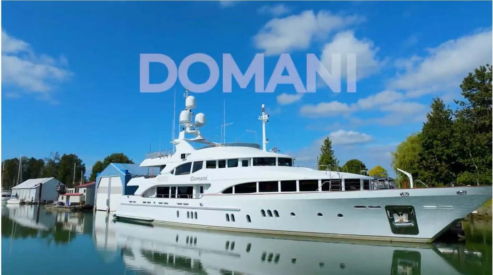 A pristine white yacht is docked in a serene marina under a clear blue sky. aboard DOMANI Yacht for Sale