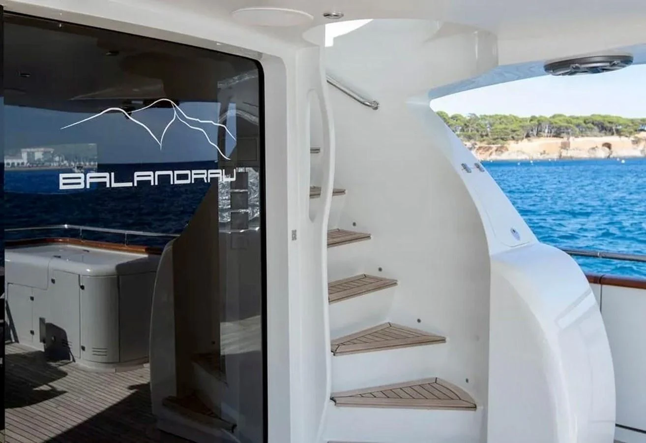 The aft deck features a staircase leading to the upper levels and a sleek glass door with the yacht's name. aboard BALANDRAU Yacht for Sale