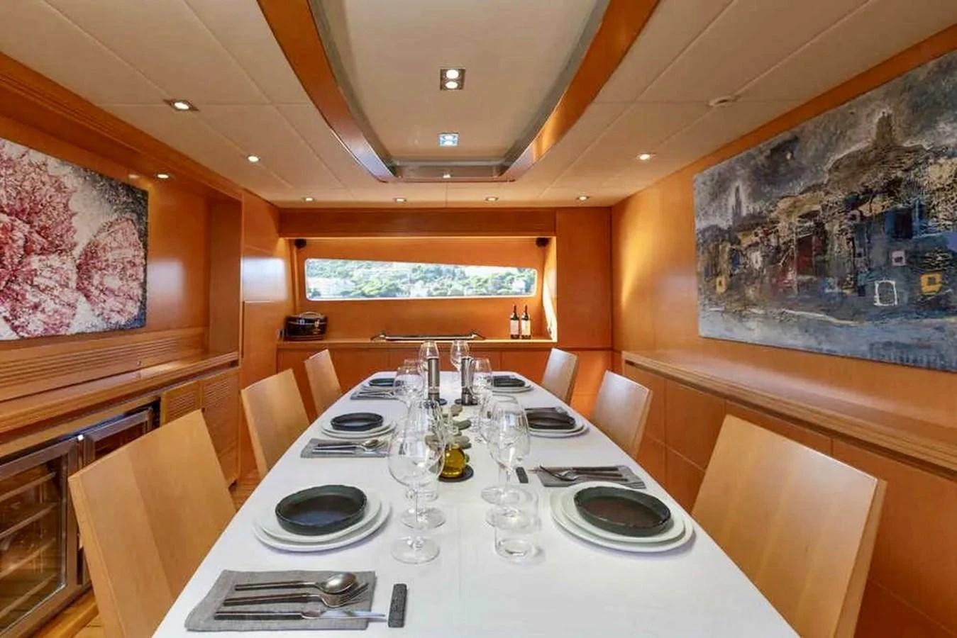 The yacht's dining area features a sleek table set for a meal, surrounded by modern decor and artwork. aboard BALANDRAU Yacht for Sale