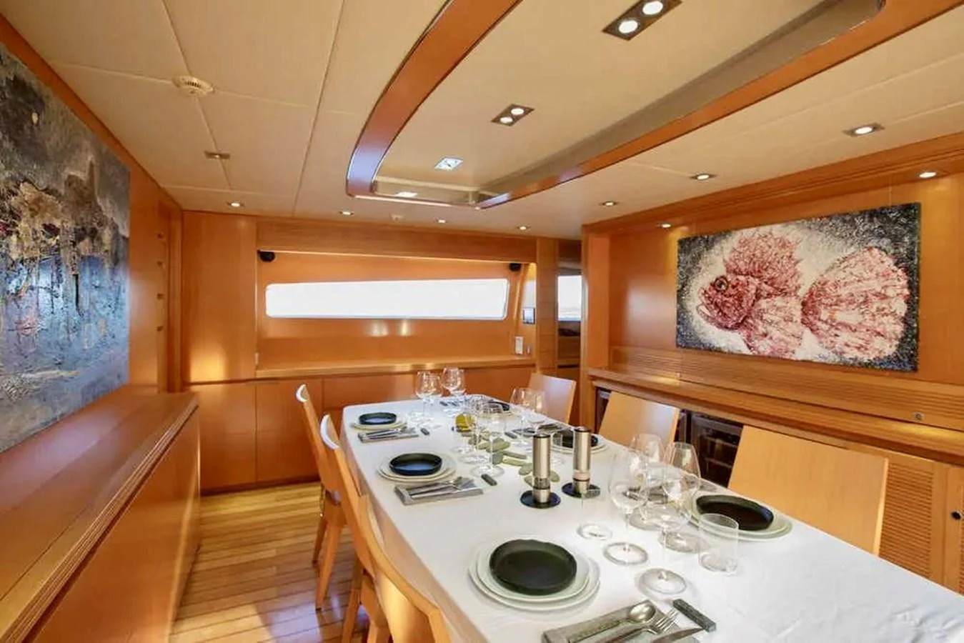 The yacht's dining area features a stylish table set for a meal, surrounded by warm wooden accents and artistic decor. aboard BALANDRAU Yacht for Sale