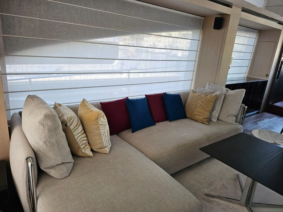 The salon features a comfortable beige sectional sofa adorned with colorful throw pillows, creating a cozy and inviting atmosphere. aboard YAS 88 Yacht for Sale