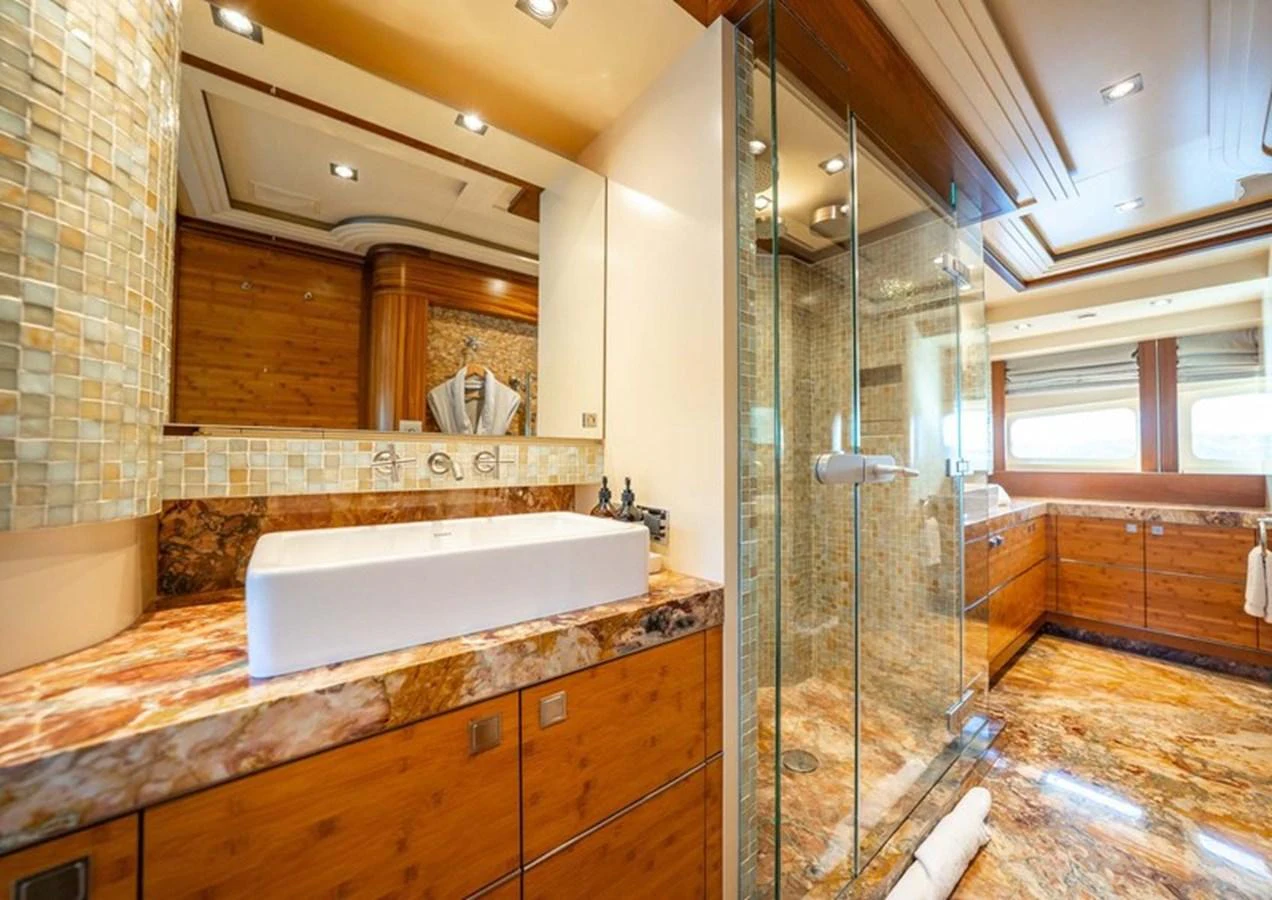 The luxurious bathroom features a spacious glass shower, elegant wood finishes, and a stylish marble countertop. aboard LUMIR Yacht for Sale
