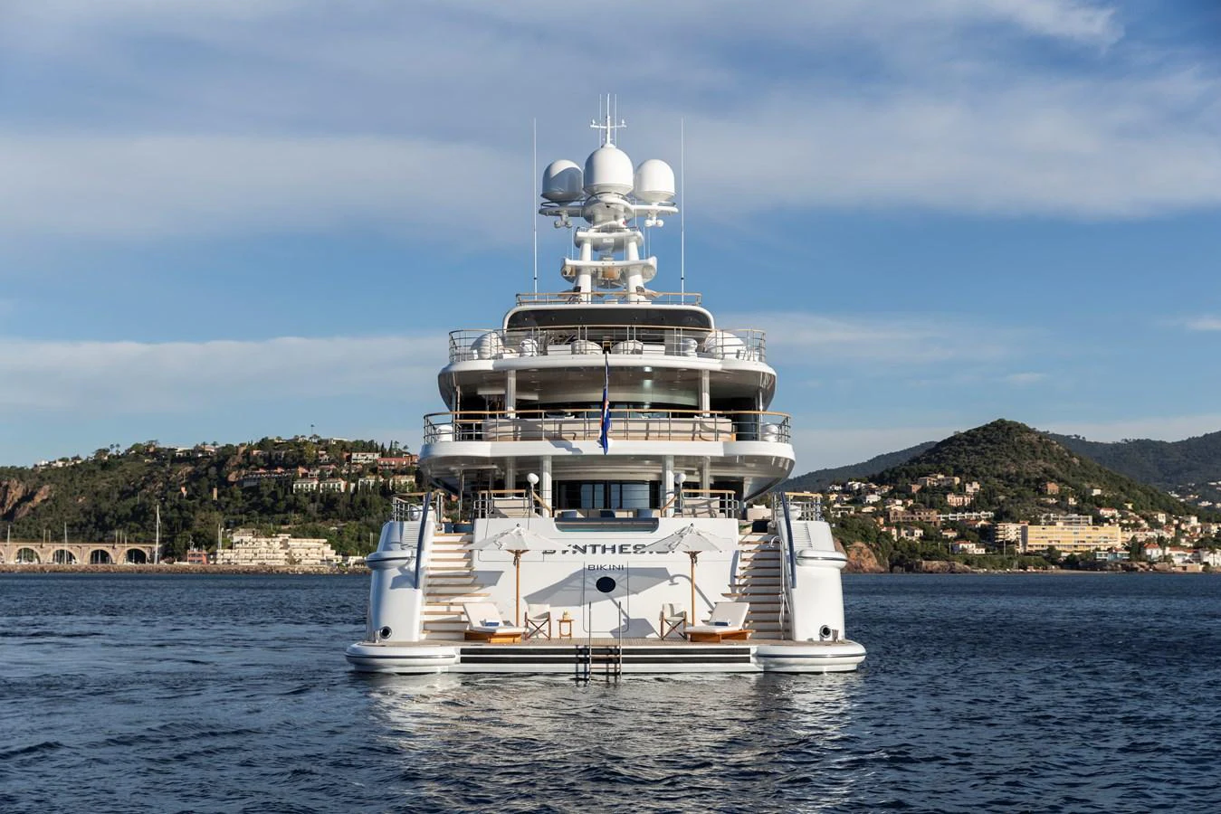 A luxurious yacht is anchored in a serene coastal area with scenic hills in the background. aboard SYNTHESIS Yacht for Sale