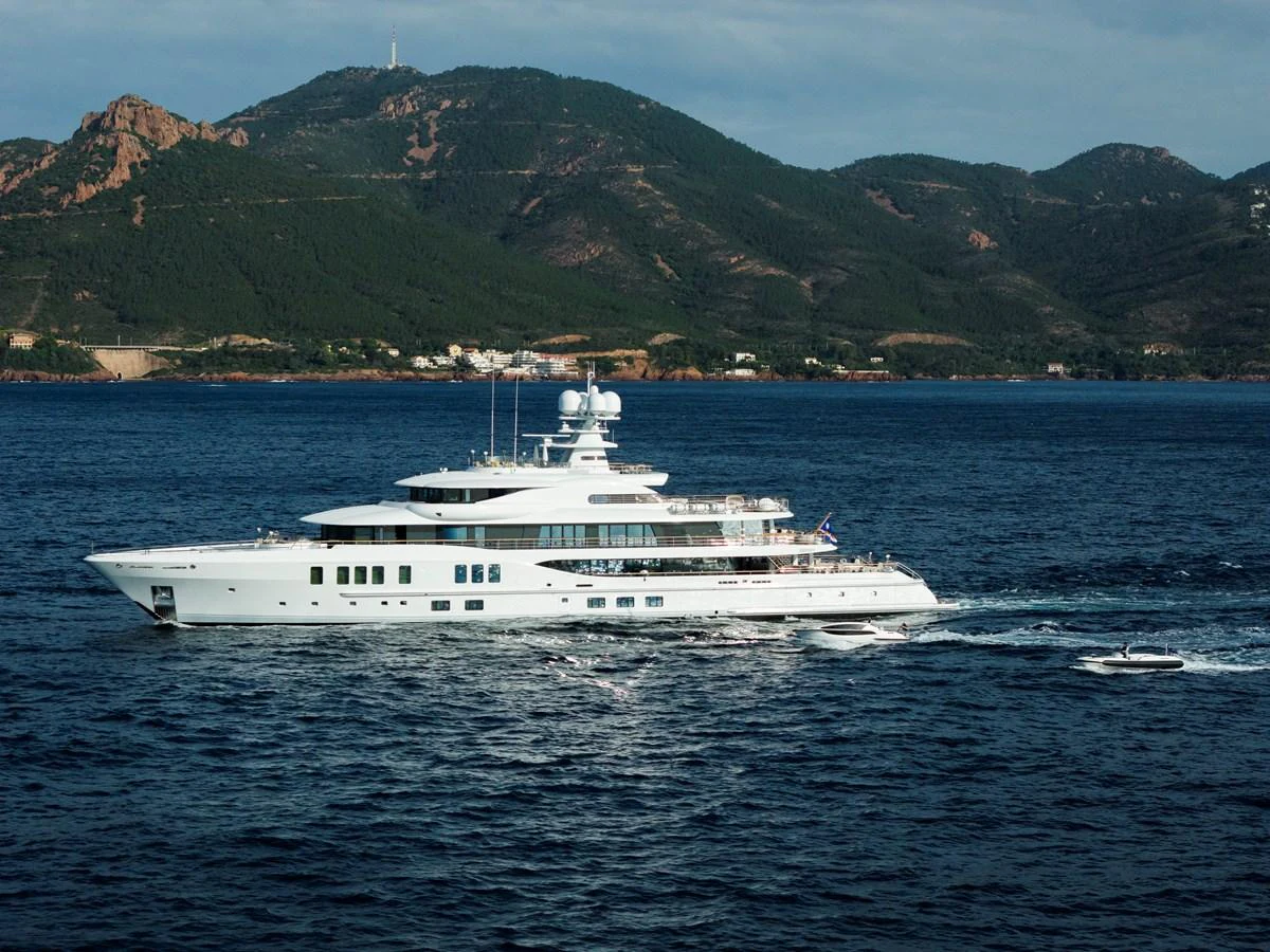 A luxurious yacht cruises along a scenic coastline with lush green hills in the background. aboard SYNTHESIS Yacht for Sale
