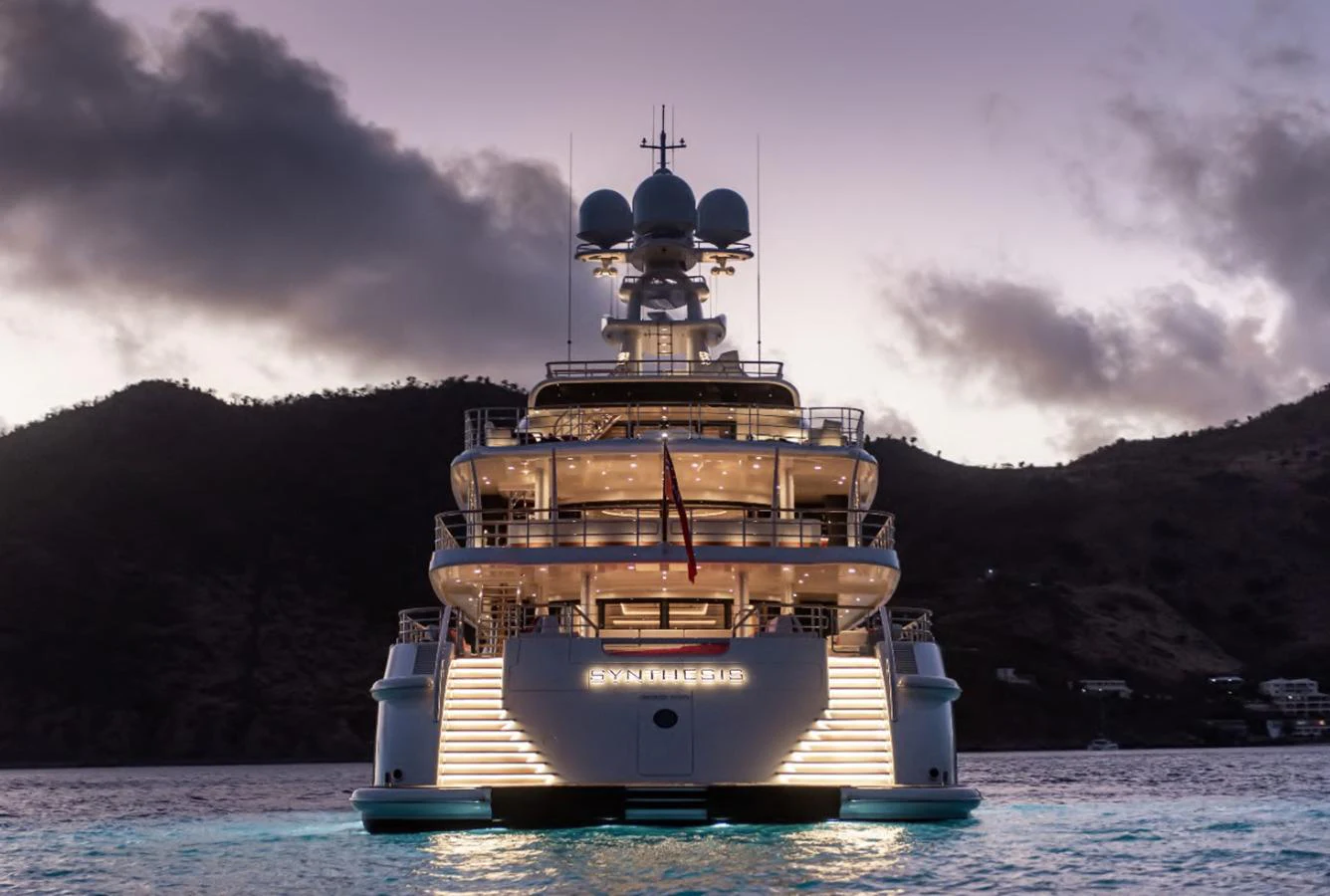 The yacht is beautifully illuminated against a twilight backdrop, showcasing its grandeur and elegance. aboard SYNTHESIS Yacht for Sale