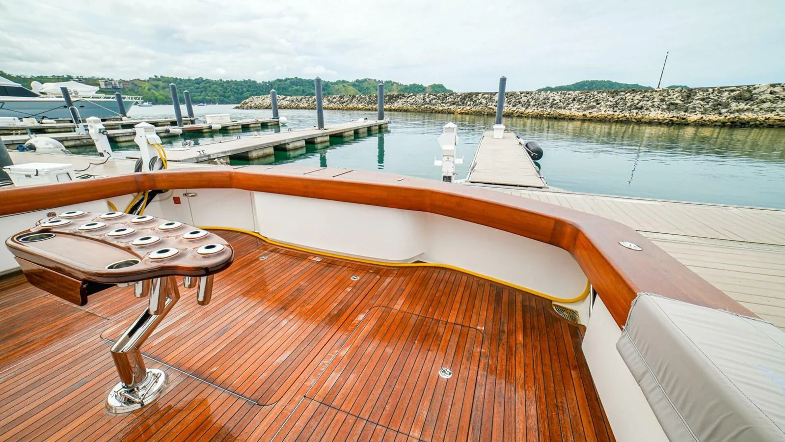 The yacht's aft deck features a polished wooden floor and a fishing rod holder, overlooking a serene marina. aboard FREE SPOOL Yacht for Sale
