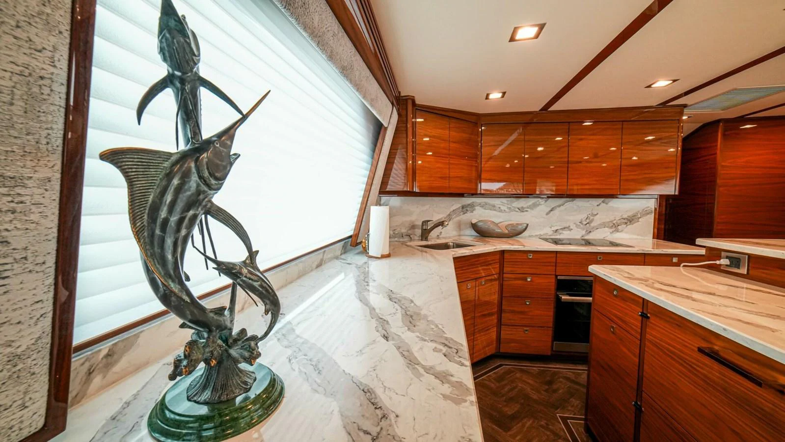 The yacht's galley features elegant wooden cabinetry and marble countertops, accented by a striking marlin sculpture. aboard FREE SPOOL Yacht for Sale