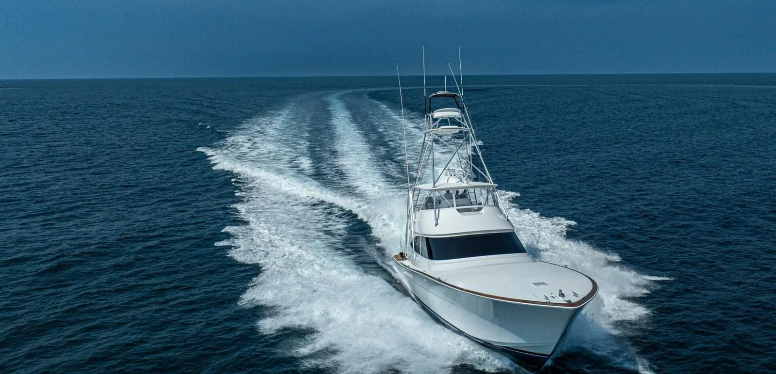 A sleek yacht cruises swiftly through open waters, leaving a trail of white wake behind. aboard FREE SPOOL Yacht for Sale