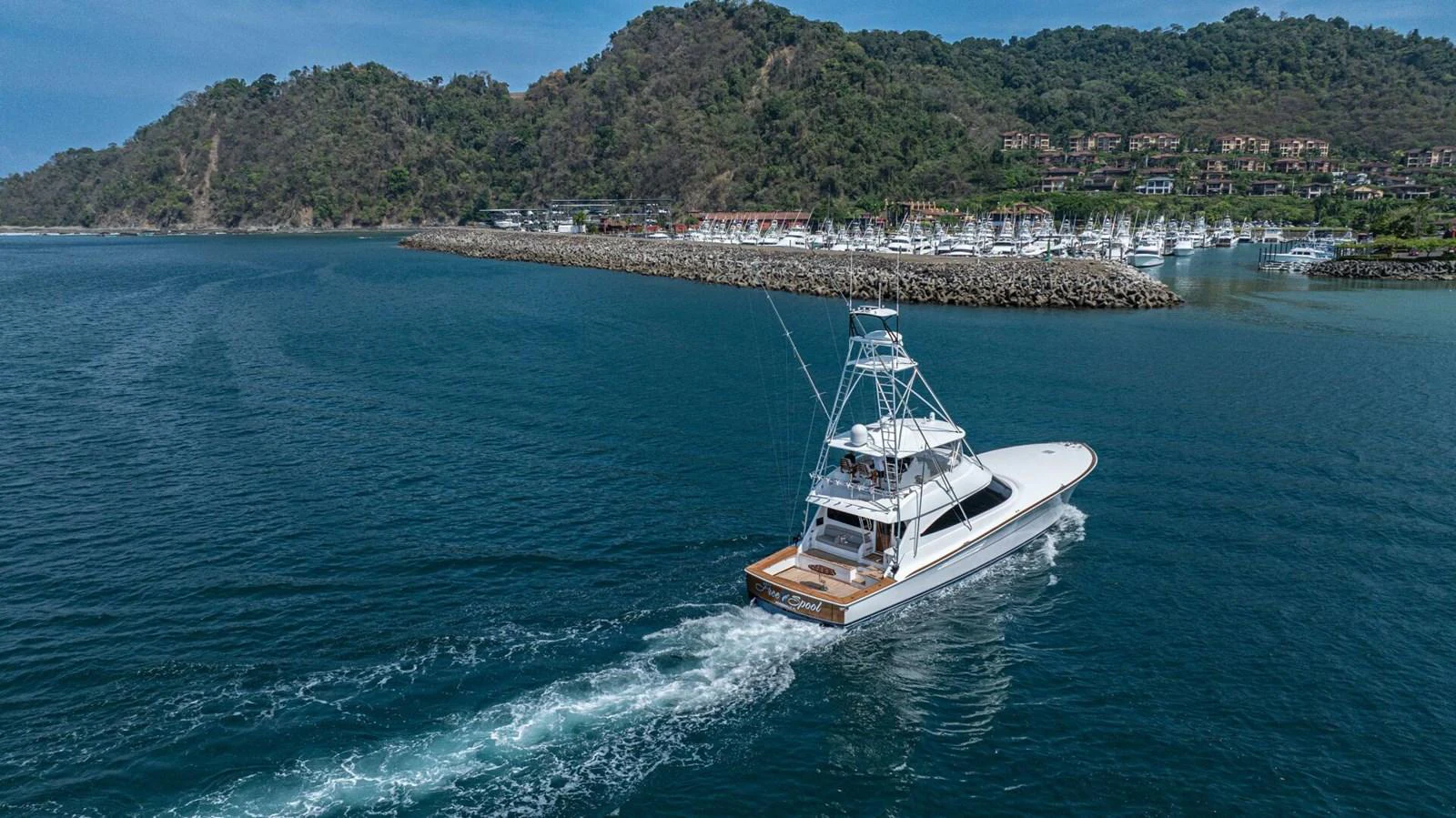 A sleek yacht cruises through calm waters near a picturesque marina and lush hills. aboard FREE SPOOL Yacht for Sale