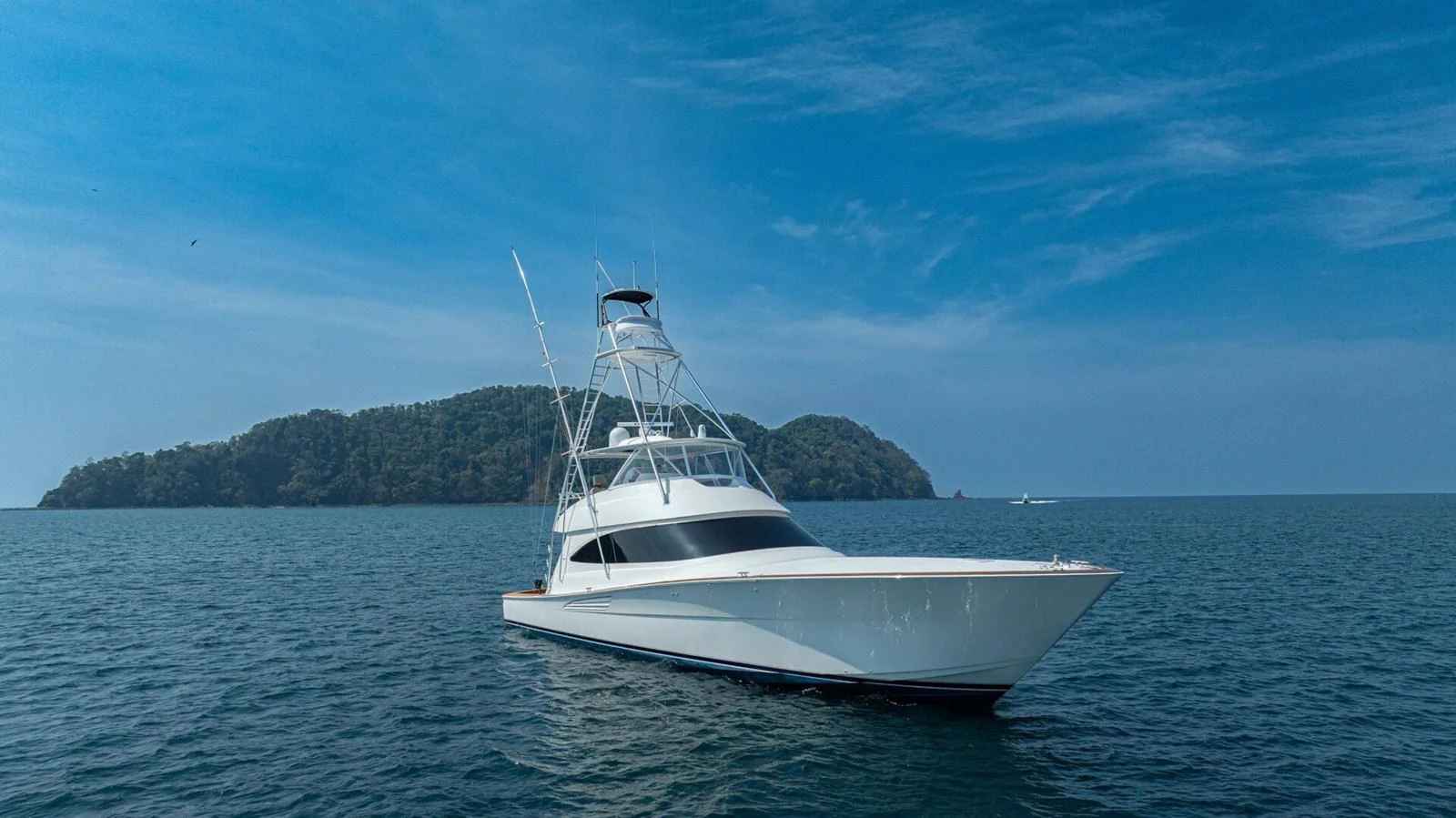 A sleek yacht glides on calm waters with a scenic island backdrop. aboard FREE SPOOL Yacht for Sale