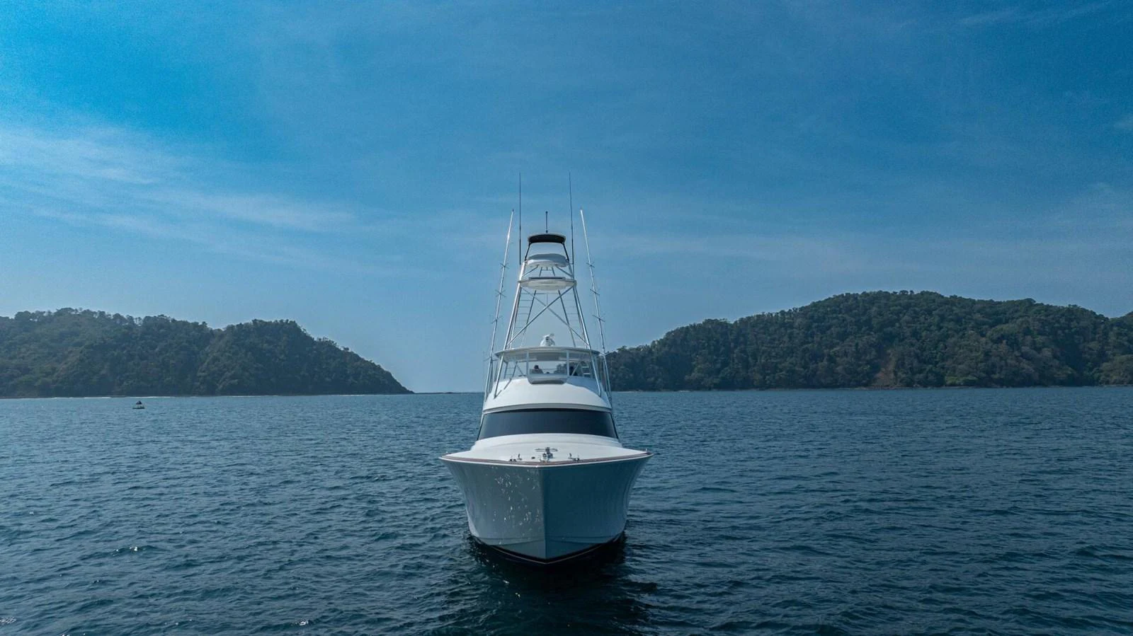 A sleek yacht is seen head-on, cruising through calm waters with scenic islands in the background. aboard FREE SPOOL Yacht for Sale