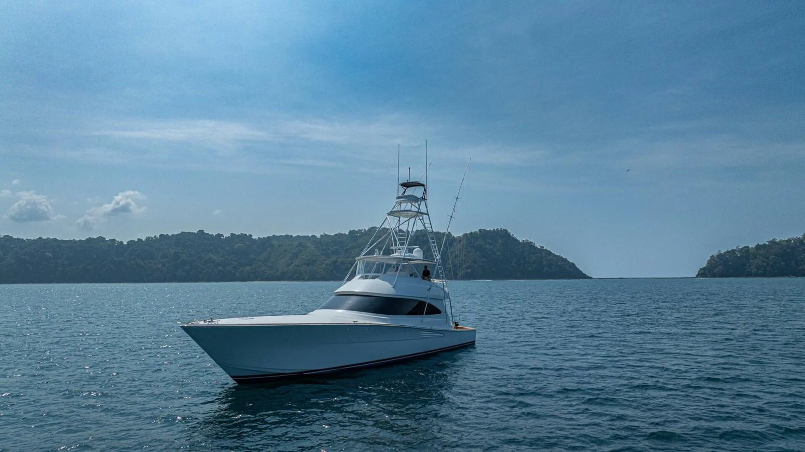 A sleek yacht cruises on calm waters with a scenic backdrop of lush islands. aboard FREE SPOOL Yacht for Sale