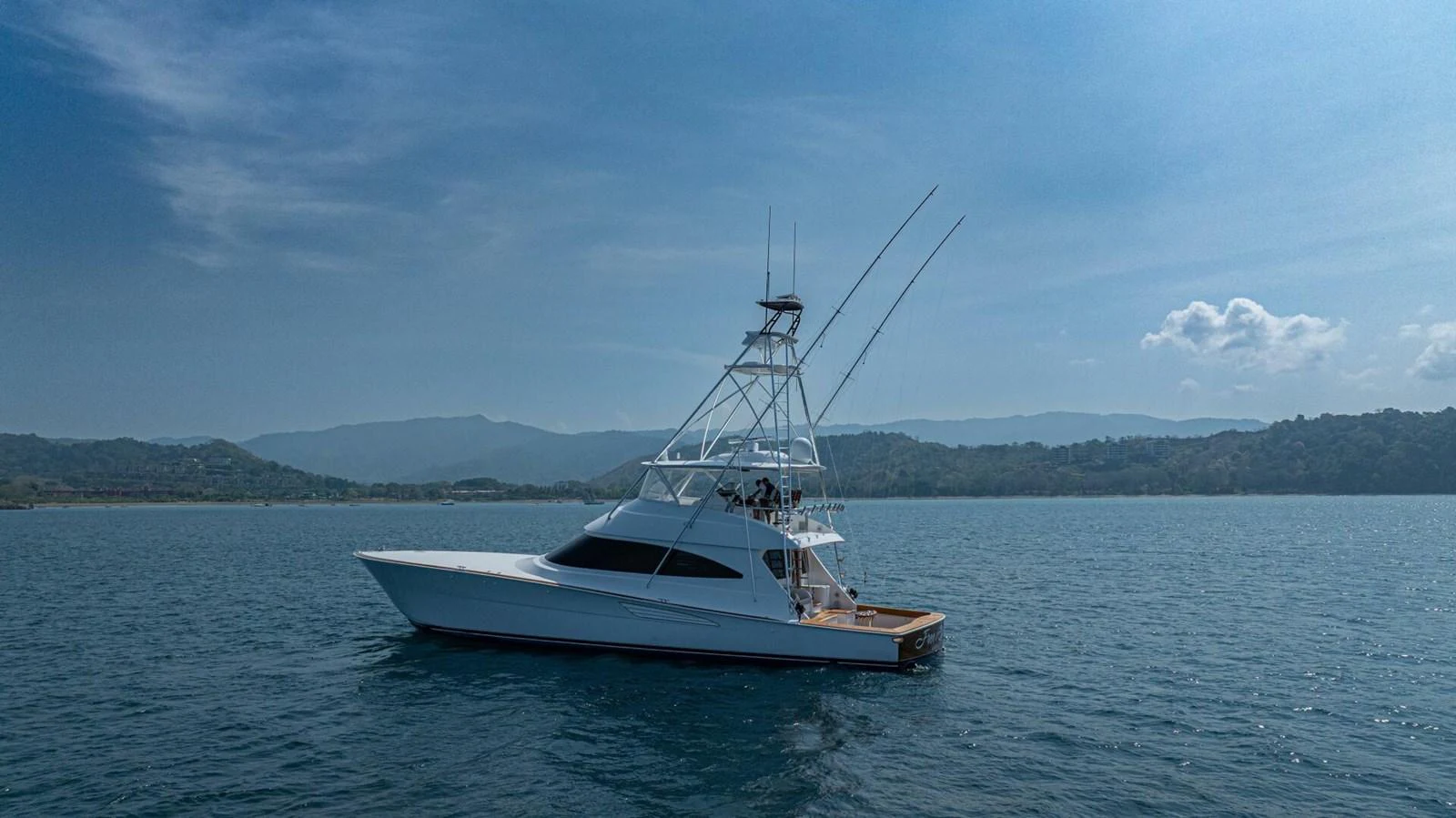 A sleek yacht glides gracefully on calm waters against a backdrop of serene mountains. aboard FREE SPOOL Yacht for Sale