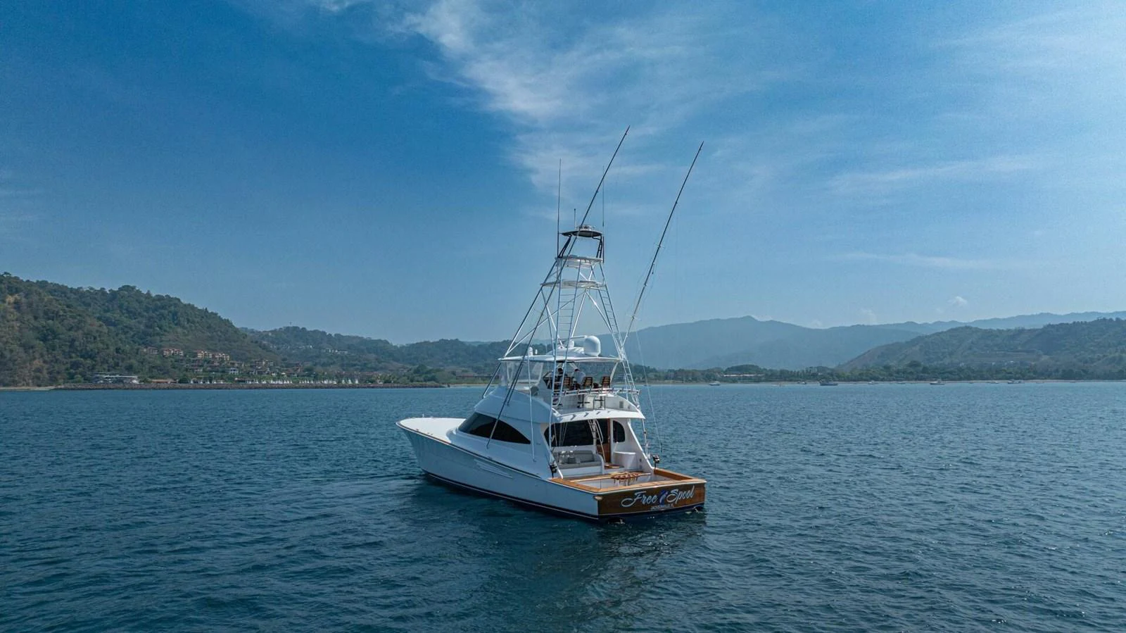 A sleek yacht cruises on calm waters with a scenic coastline in the background. aboard FREE SPOOL Yacht for Sale