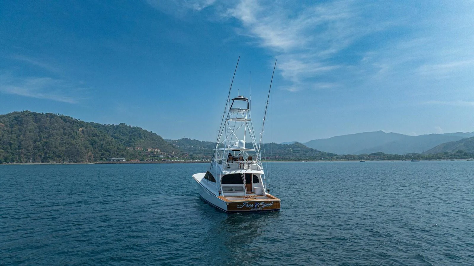 A sleek yacht is anchored on calm waters with scenic hills in the background. aboard FREE SPOOL Yacht for Sale