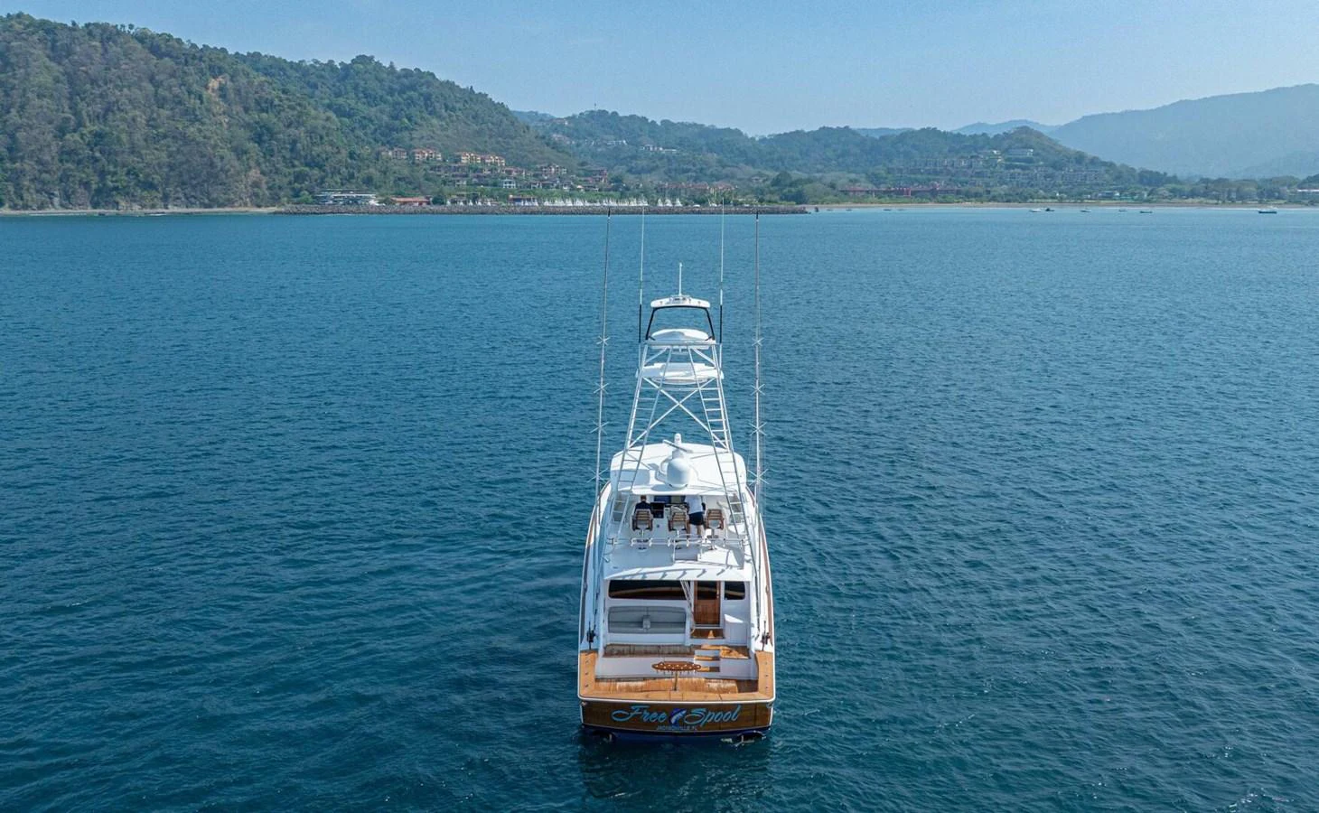 A sleek yacht cruises on calm waters with a scenic coastline in the background. aboard FREE SPOOL Yacht for Sale