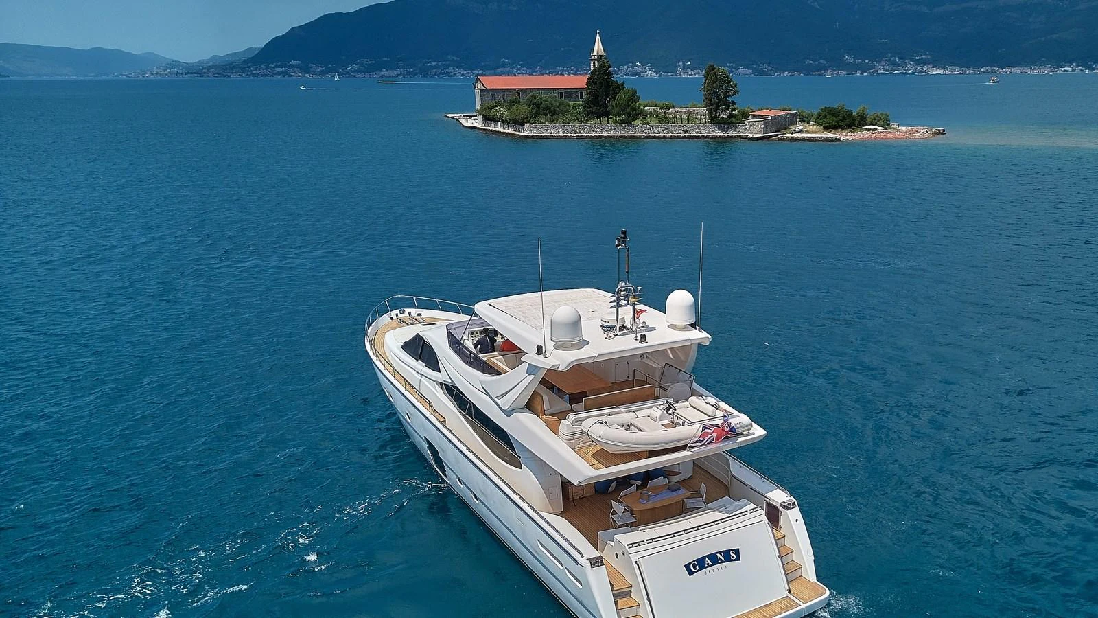 A sleek yacht cruises near a picturesque island in clear blue waters. aboard GANS Yacht for Sale
