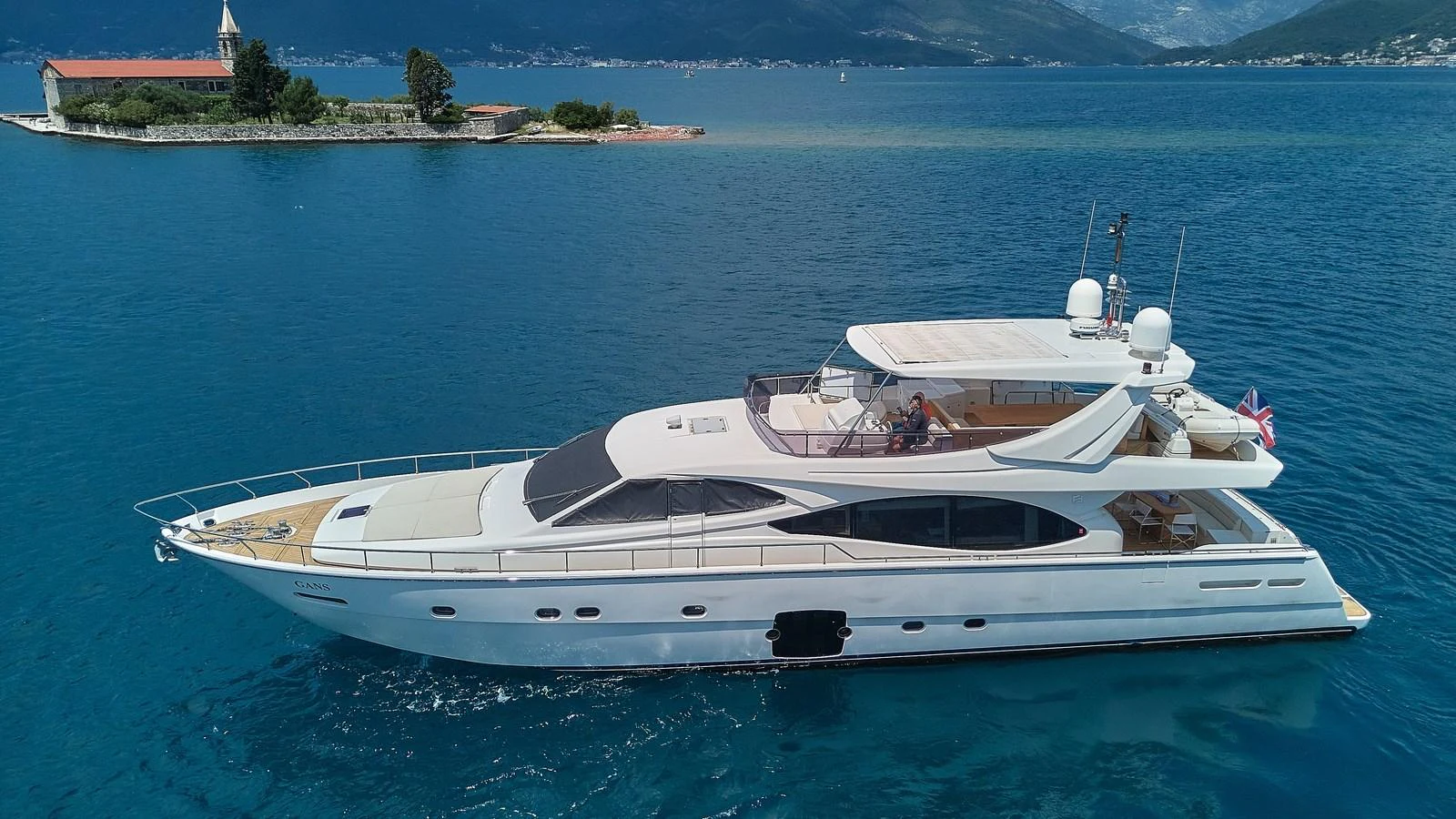 A sleek yacht glides through calm waters near a picturesque island. aboard GANS Yacht for Sale
