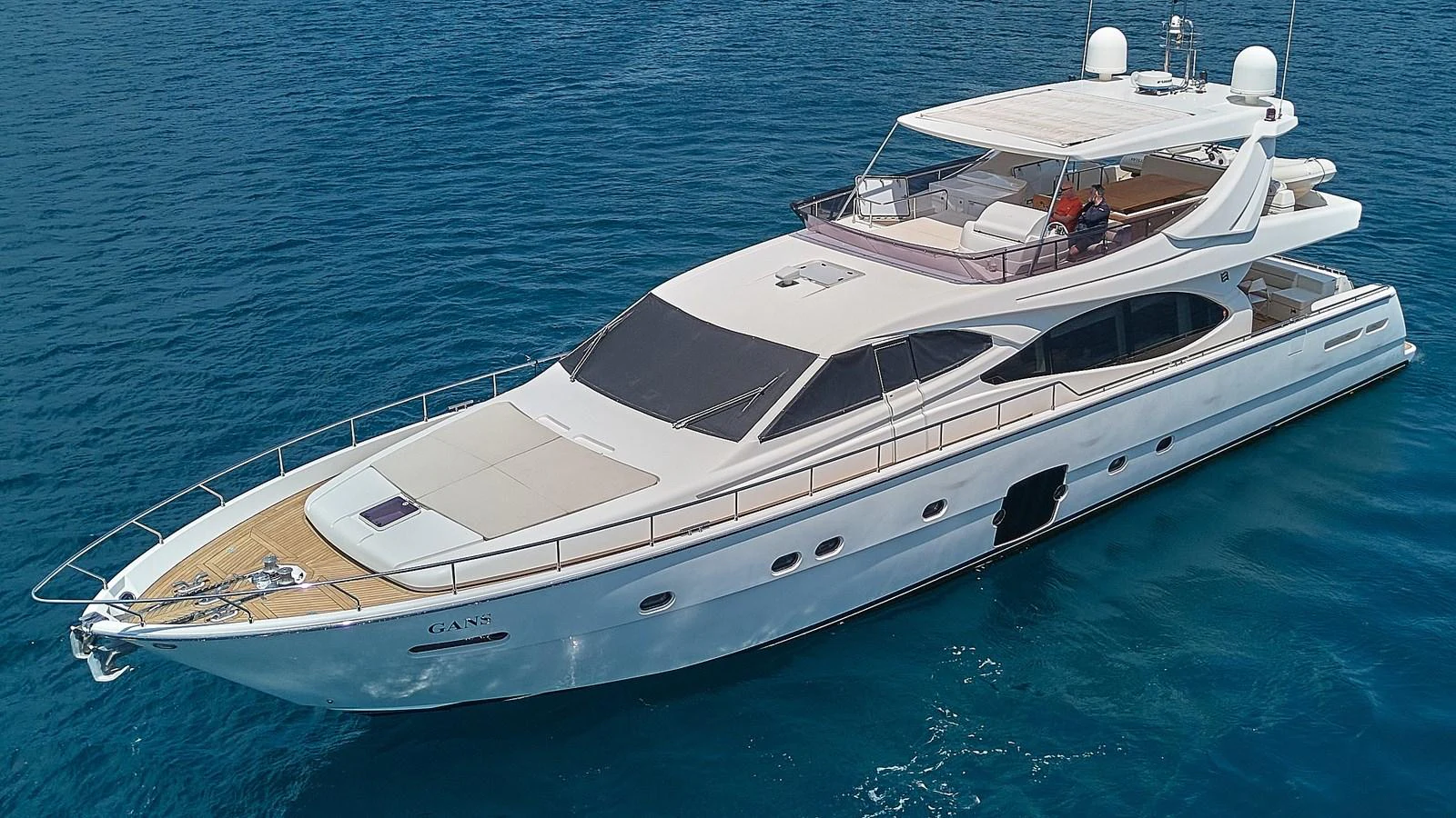A sleek white yacht cruises on clear blue waters, showcasing its elegant design and spacious deck areas. aboard GANS Yacht for Sale