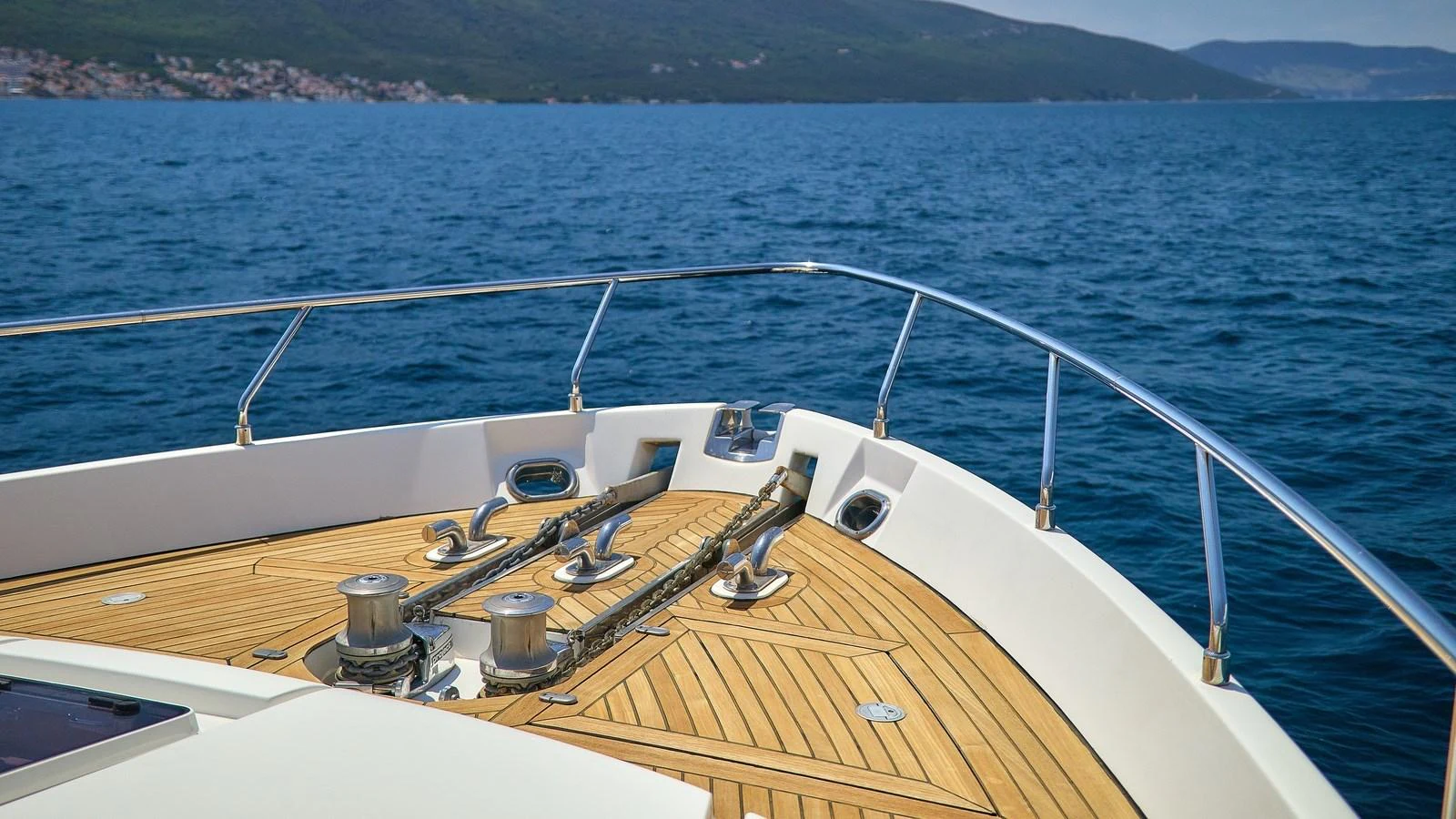 The foredeck showcases polished hardware and a sleek wooden finish against a stunning ocean backdrop. aboard GANS Yacht for Sale