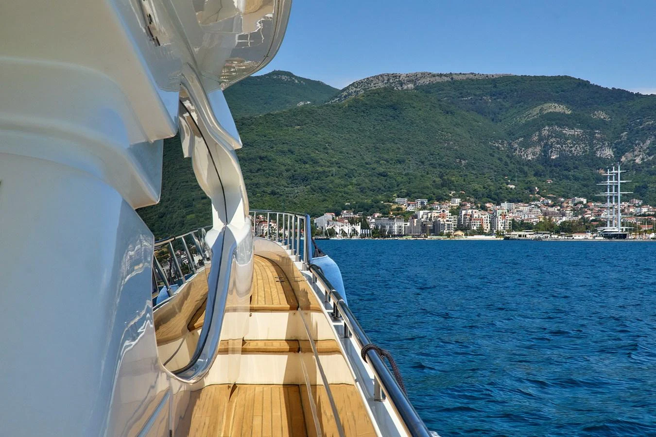 The yacht cruises along a scenic coastline with lush hills and a charming town in the background. aboard GANS Yacht for Sale