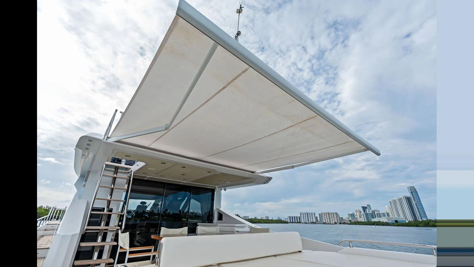 The aft deck features a retractable sunshade, offering a comfortable outdoor lounging area with a view of the city skyline. aboard VILLAGGIO Yacht for Sale