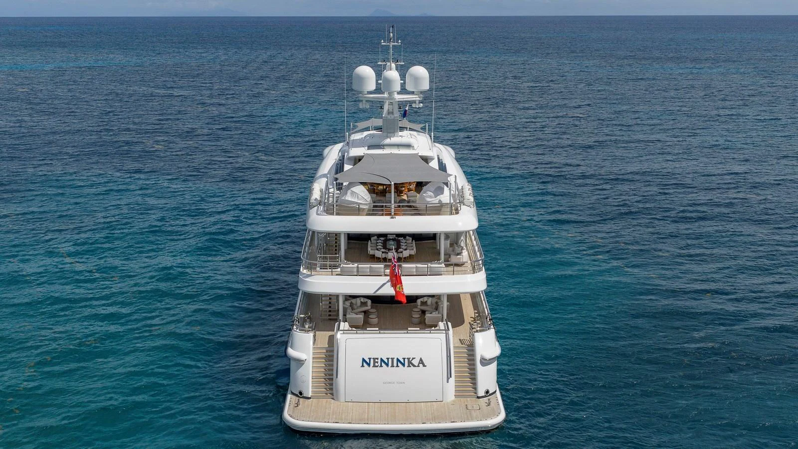 A luxurious yacht is anchored in serene blue waters, showcasing its elegant design from the rear view. aboard NENINKA Yacht for Sale