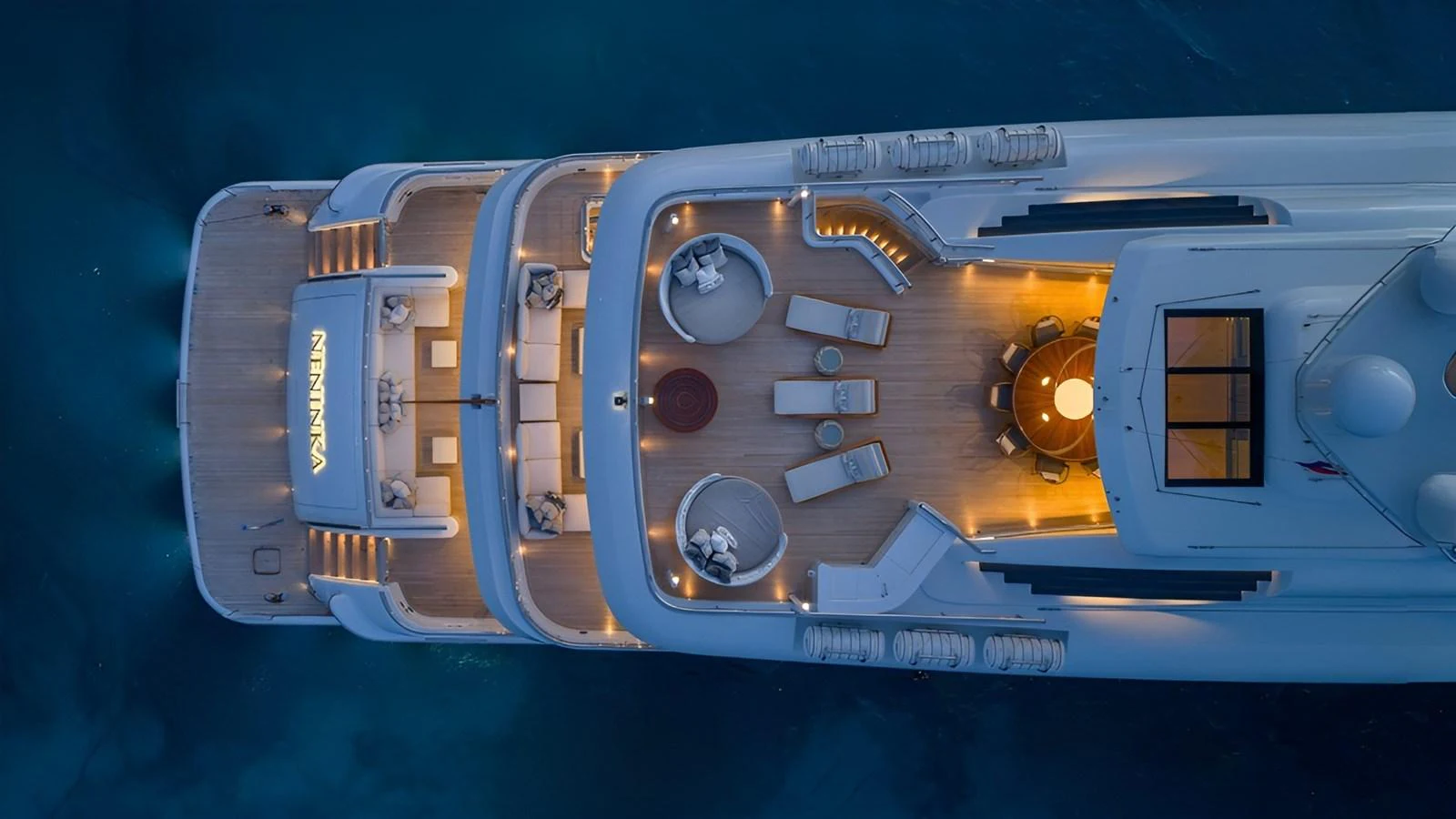 An aerial view of a yacht's sundeck illuminated at dusk, showcasing luxurious lounging areas. aboard NENINKA Yacht for Sale