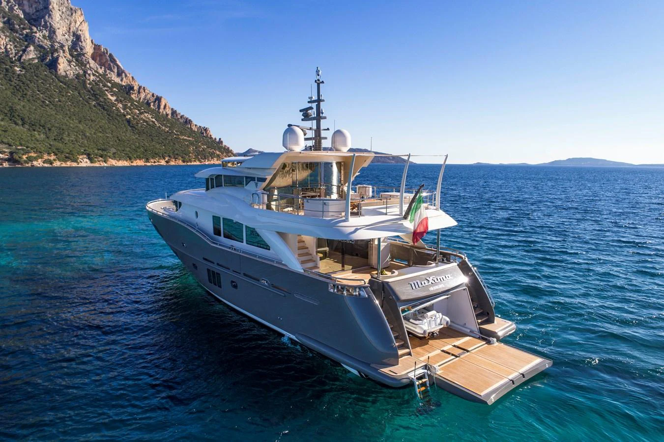 A sleek and modern yacht cruising in clear blue waters with a stunning coastal backdrop. aboard MAXIMA Yacht for Sale