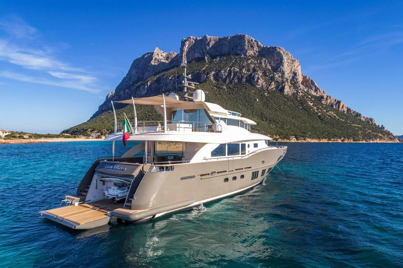 A luxurious yacht cruises in pristine blue waters with a stunning mountainous backdrop. aboard MAXIMA Yacht for Sale