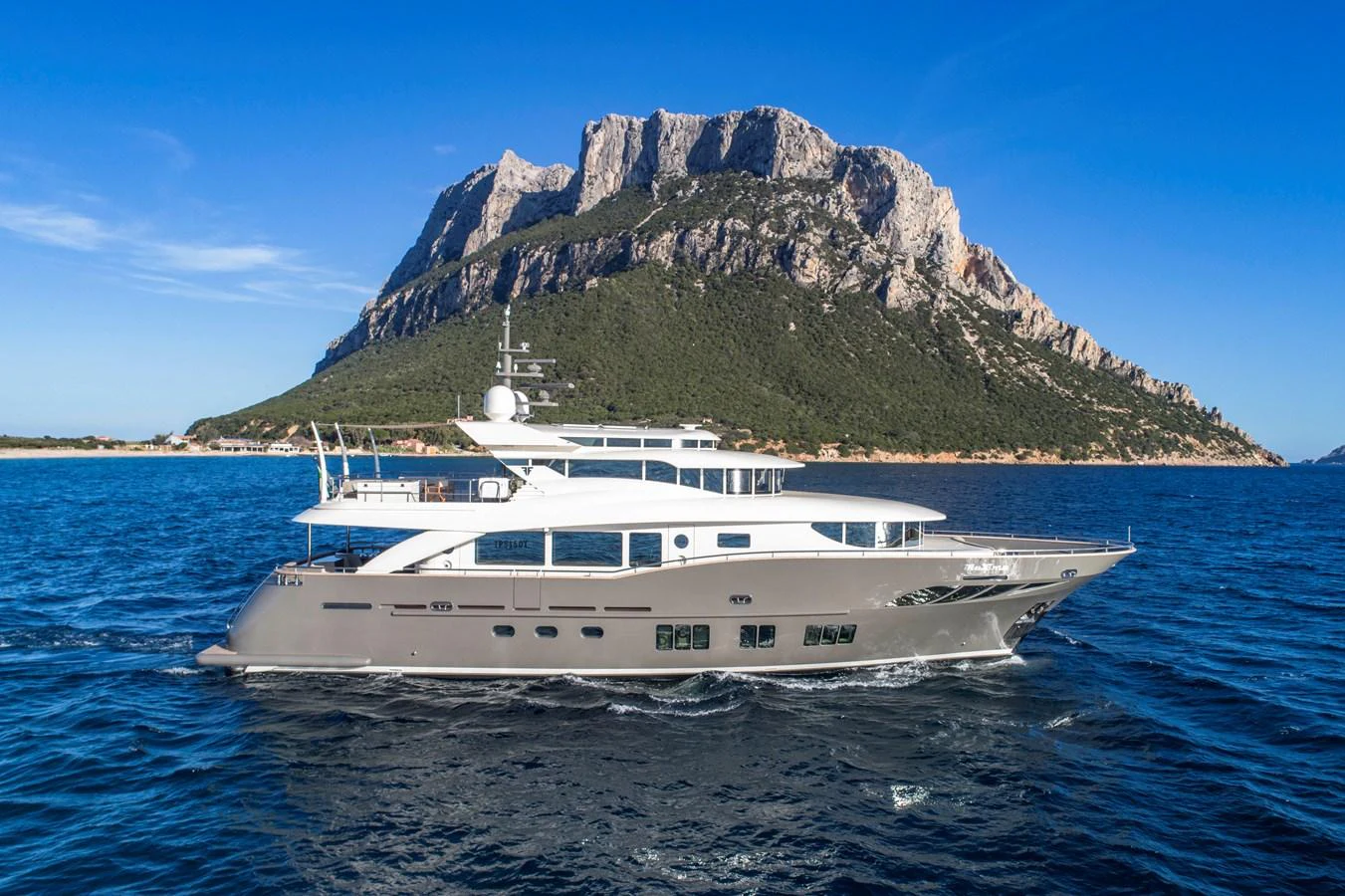 A sleek yacht cruises in front of a stunning mountainous backdrop on a clear day. aboard MAXIMA Yacht for Sale