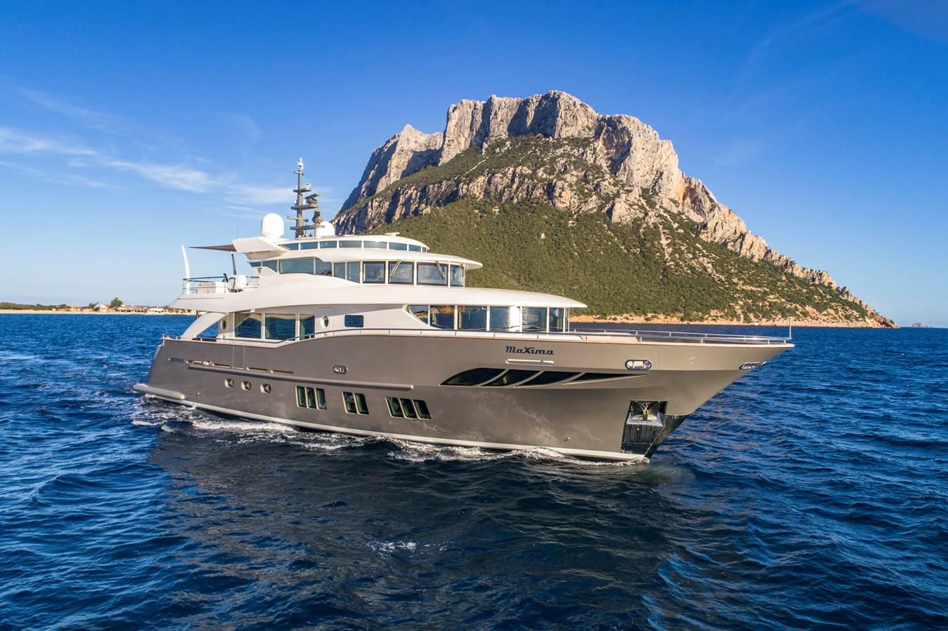 A sleek and modern yacht cruising in clear blue waters with a stunning mountainous backdrop. aboard MAXIMA Yacht for Sale