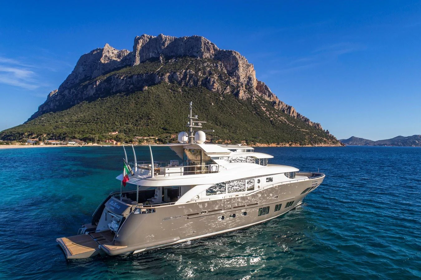 A luxurious yacht cruises along a stunning coastal landscape with a mountainous backdrop. aboard MAXIMA Yacht for Sale