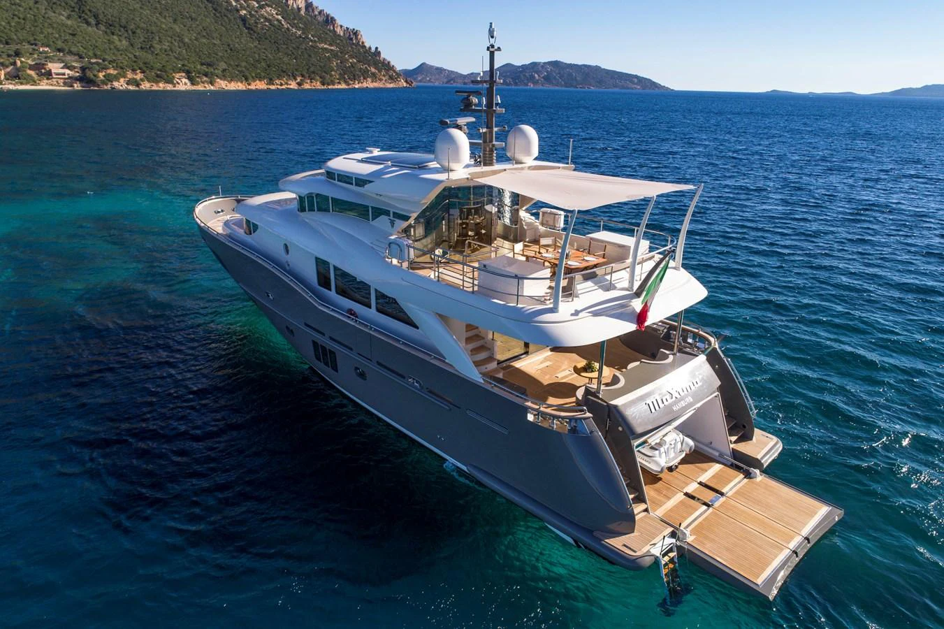 A sleek and modern yacht cruising in clear blue waters with a scenic coastline in the background. aboard MAXIMA Yacht for Sale